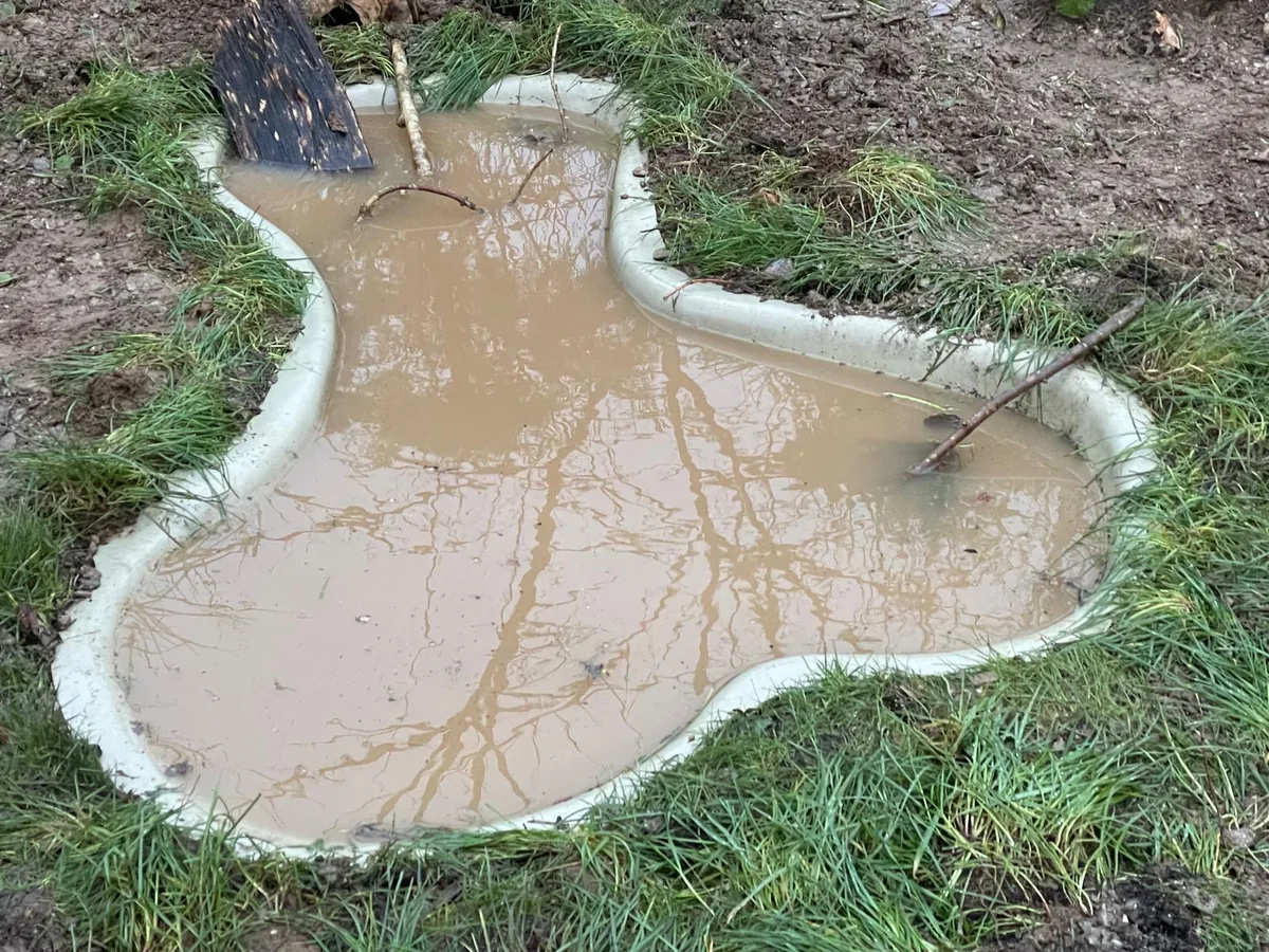 A newly sunk wildlife pond on day one: a preformed shell filled with cloudy water in a bare patch of garden